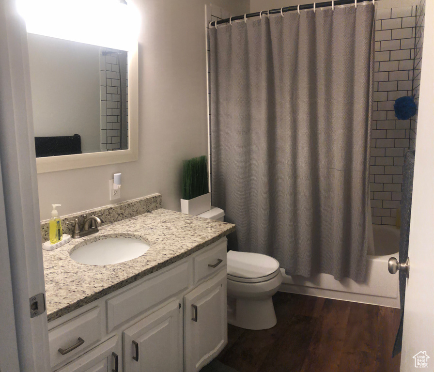 Full bathroom with vanity with extensive cabinet space, hardwood / wood-style flooring, shower / tub combo, and toilet