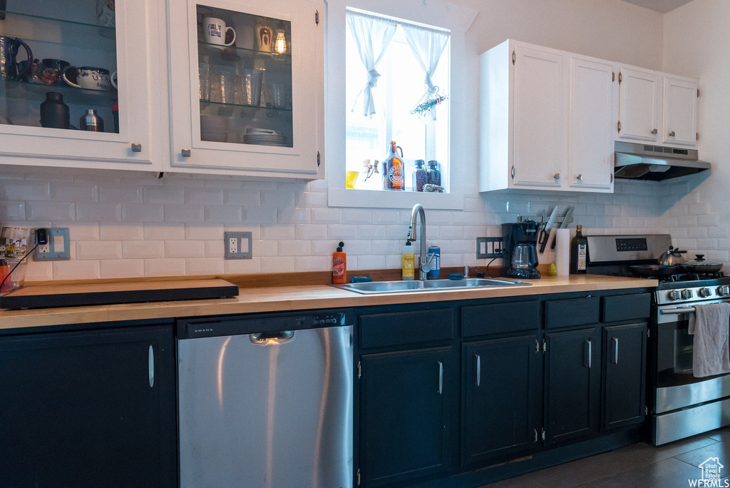 Kitchen featuring sink, backsplash, dark tile flooring, white cabinetry, and stainless steel appliances