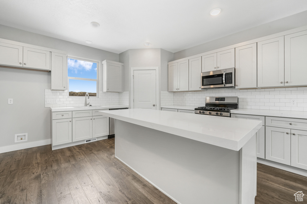 Kitchen with white cabinetry, dark hardwood / wood-style flooring, backsplash, a kitchen island, and stainless steel appliances