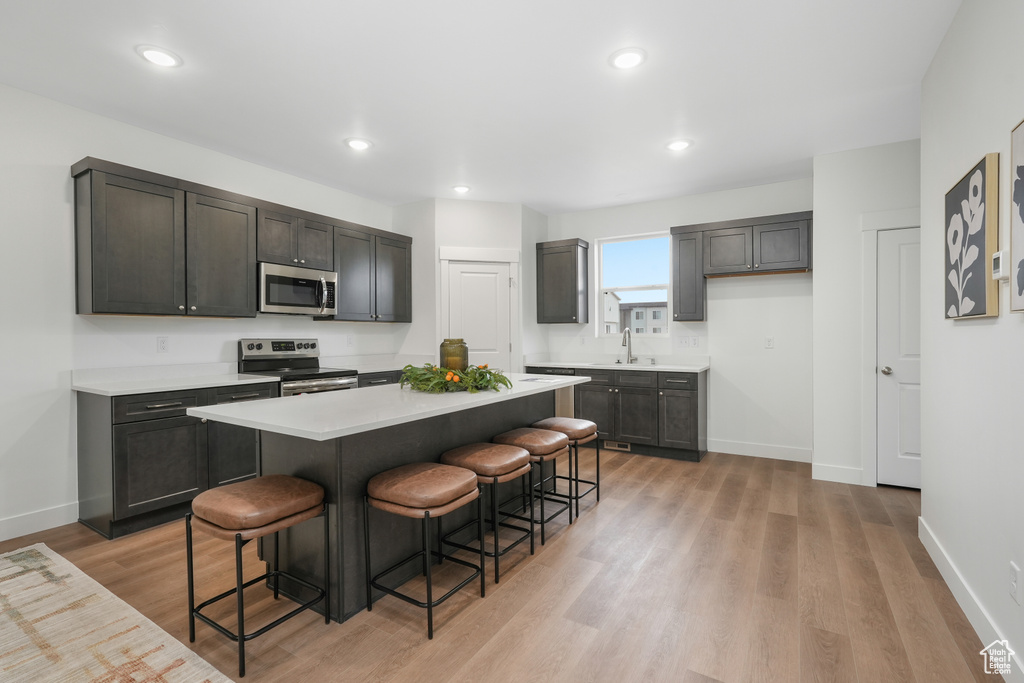 Kitchen with stainless steel appliances, sink, a breakfast bar, light hardwood / wood-style flooring, and a kitchen island