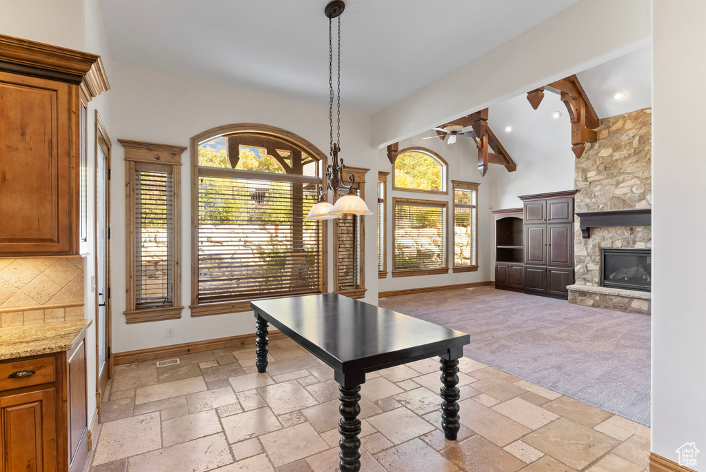 Interior space featuring a fireplace, ceiling fan, light carpet, and vaulted ceiling with beams