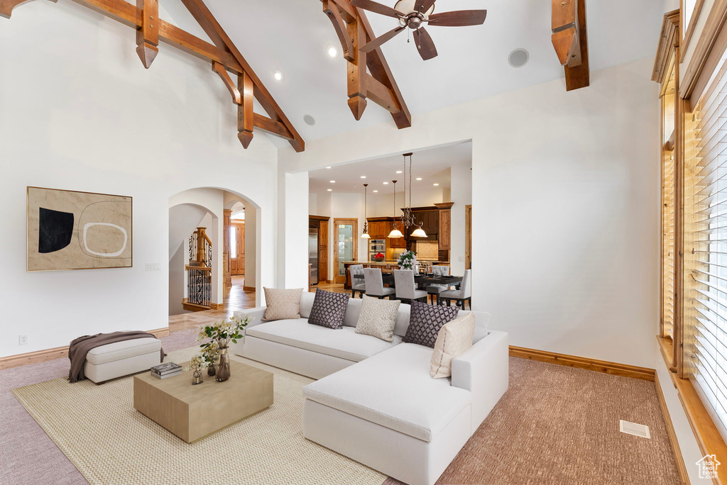 Carpeted living room with high vaulted ceiling, beamed ceiling, and ceiling fan