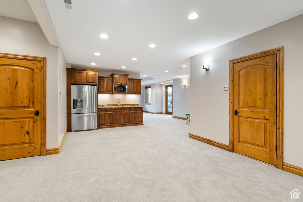 Kitchen with stainless steel appliances, light carpet, and light stone counters
