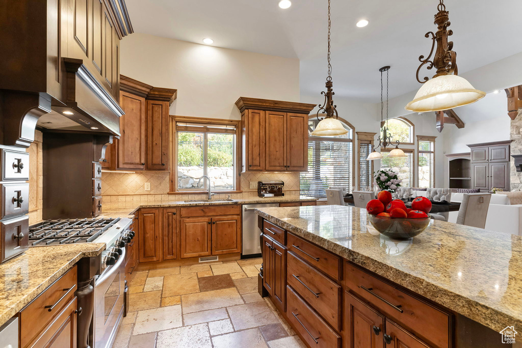 Kitchen featuring sink, light stone counters, appliances with stainless steel finishes, tasteful backsplash, and decorative light fixtures