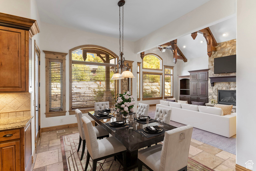 Dining space with ceiling fan, a stone fireplace, and lofted ceiling with beams