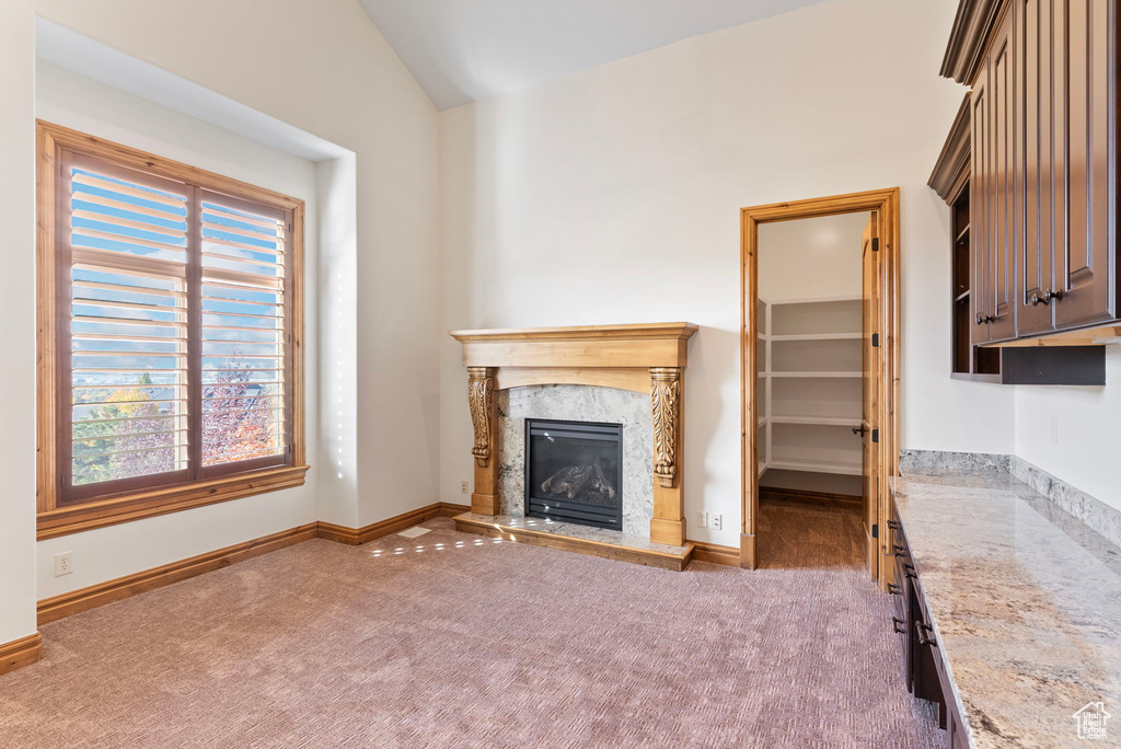 Unfurnished living room featuring dark colored carpet, vaulted ceiling, and a premium fireplace