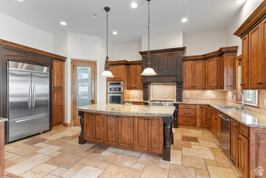 Kitchen with sink, light stone counters, hanging light fixtures, a center island, and premium appliances