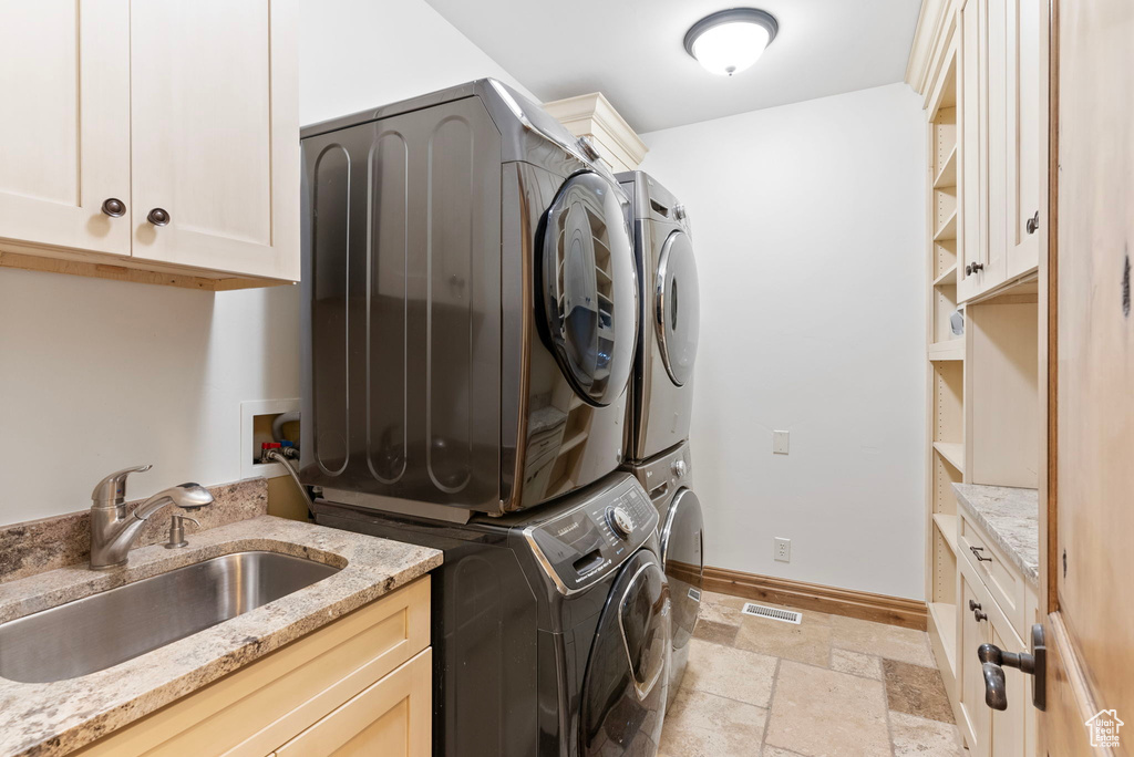 Laundry area with cabinets, sink, and stacked washer and dryer