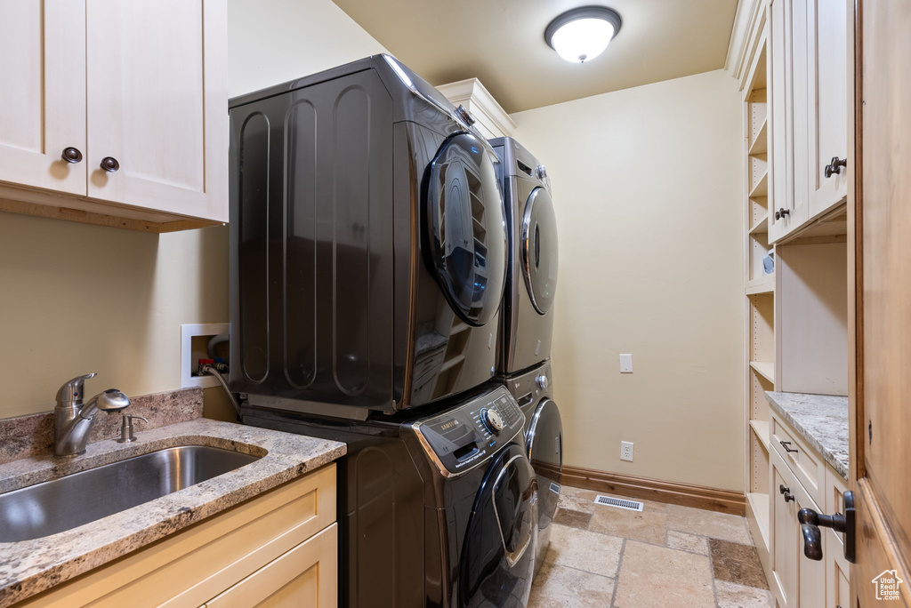 Washroom with sink, stacked washer / drying machine, washer hookup, light tile floors, and cabinets