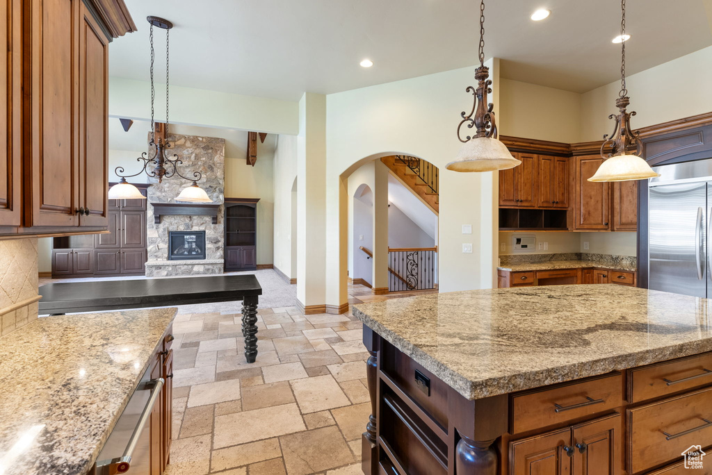 Kitchen featuring hanging light fixtures, tasteful backsplash, light stone countertops, light tile floors, and a stone fireplace