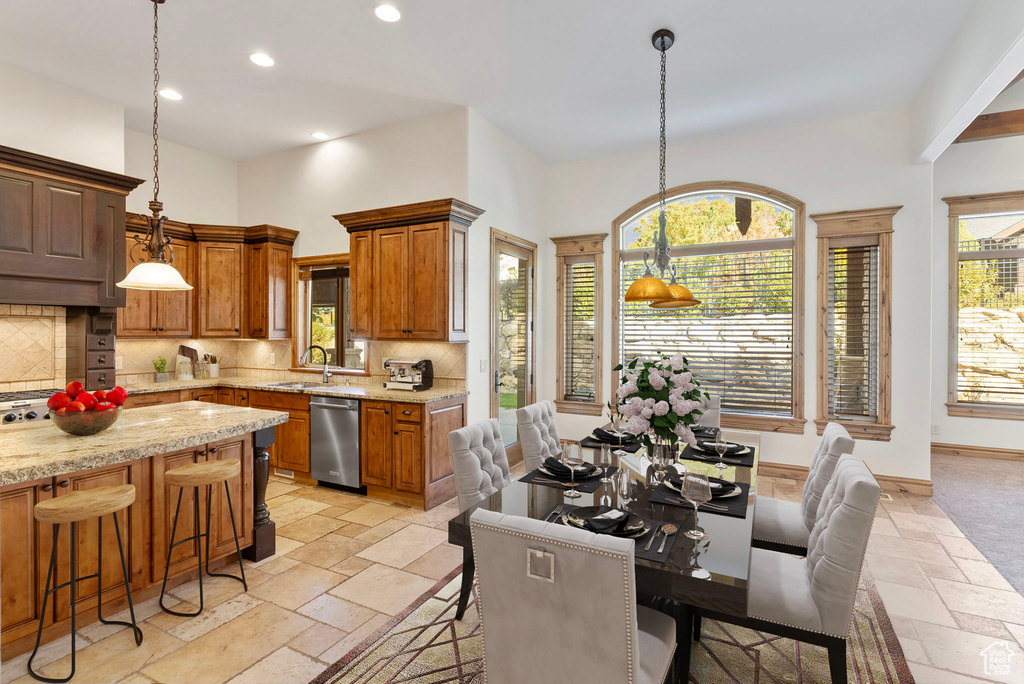 Kitchen with light stone counters, backsplash, hanging light fixtures, sink, and stainless steel dishwasher