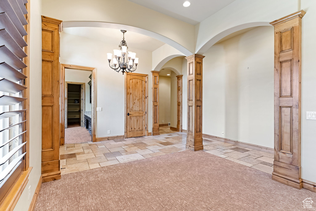 Entryway with light colored carpet, a notable chandelier, and decorative columns