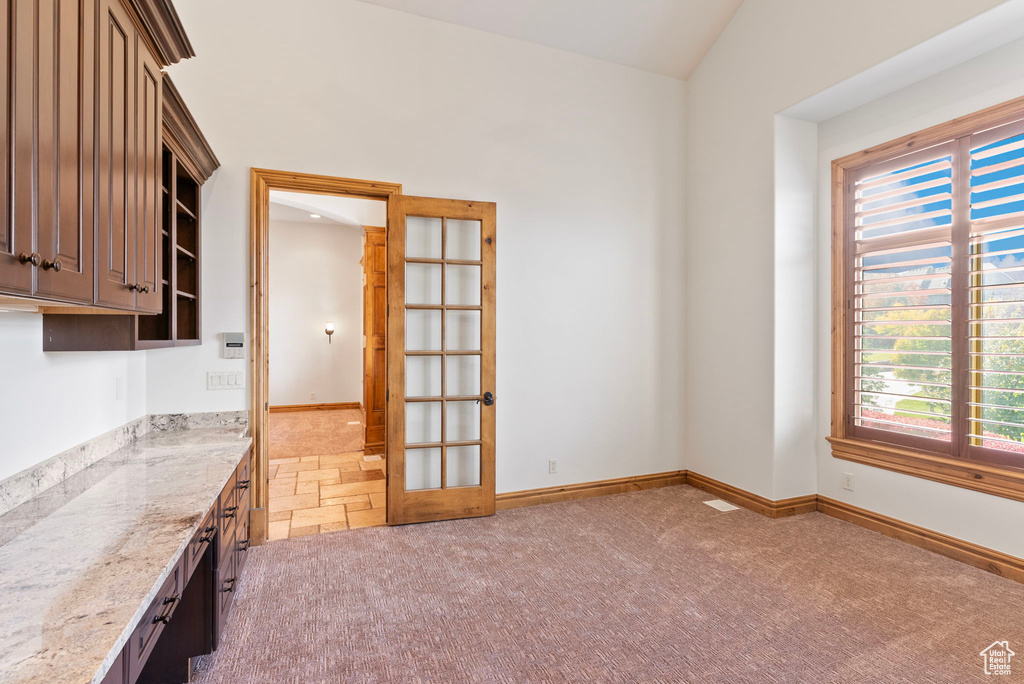 Interior space featuring vaulted ceiling, dark brown cabinets, light stone counters, and carpet floors