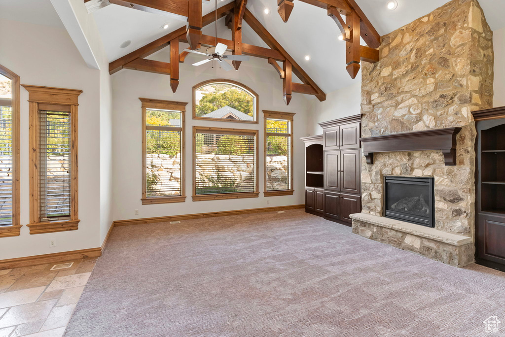 Unfurnished living room featuring beamed ceiling, ceiling fan, a stone fireplace, and high vaulted ceiling