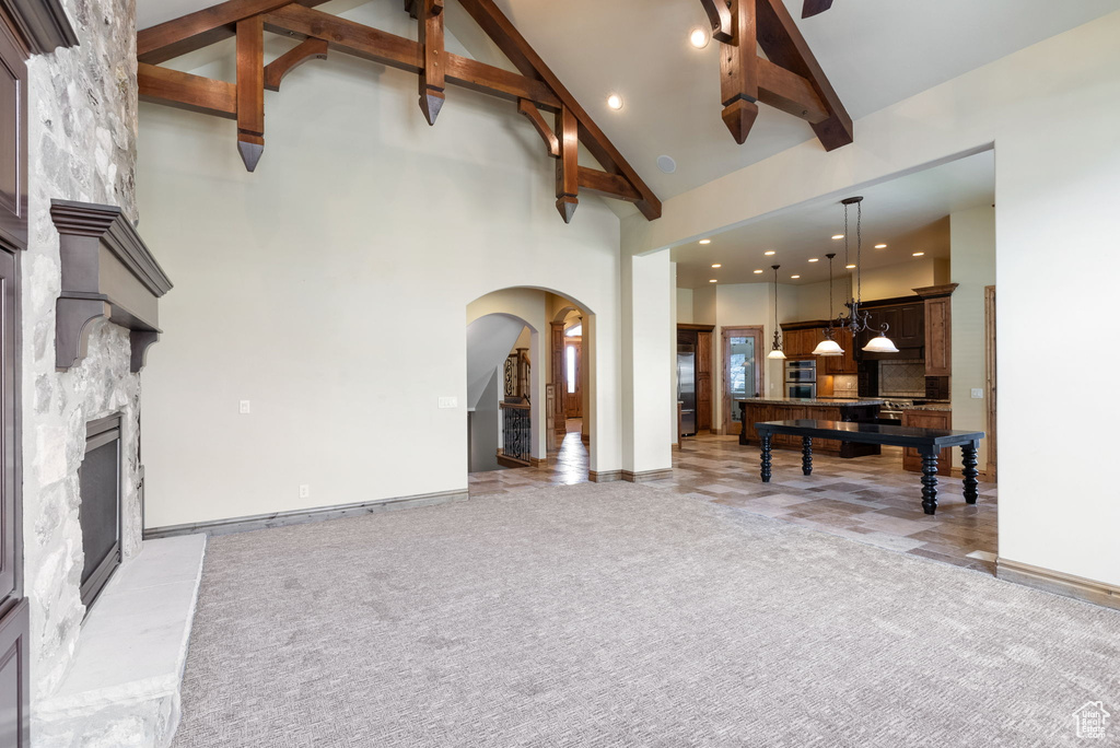 Carpeted living room with high vaulted ceiling, beamed ceiling, and a fireplace