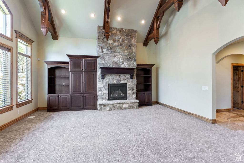 Unfurnished living room featuring light colored carpet, a fireplace, beam ceiling, and plenty of natural light