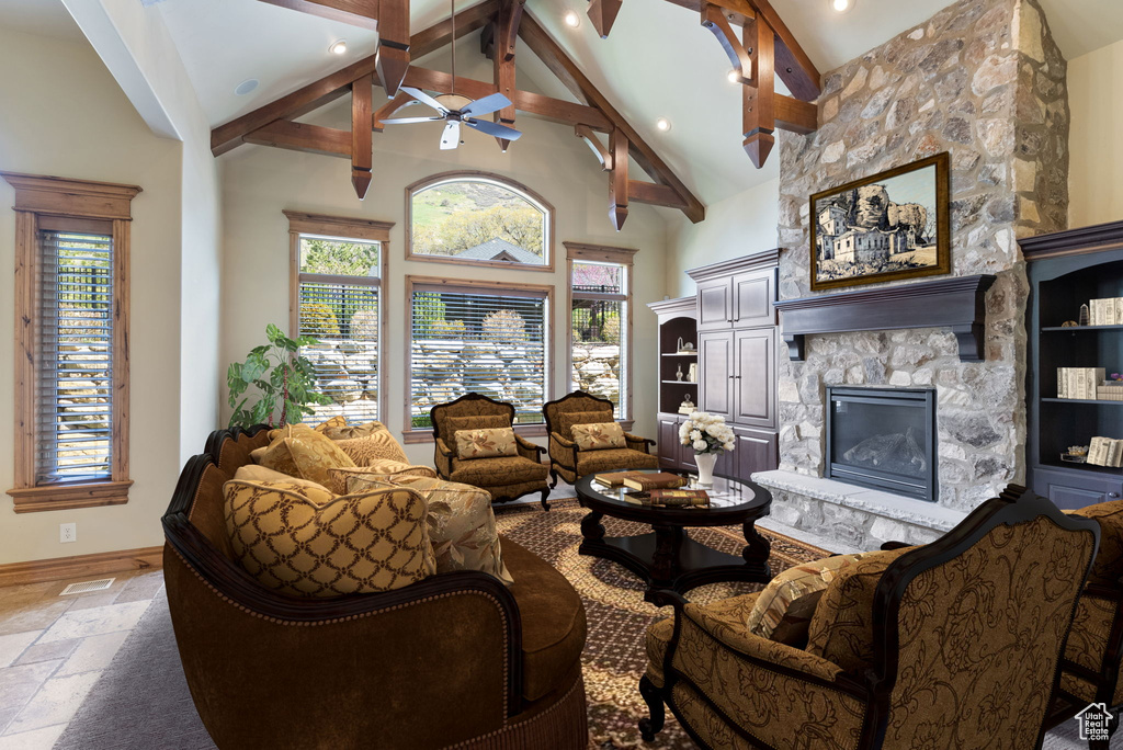 Tiled living room featuring high vaulted ceiling, beamed ceiling, built in features, a stone fireplace, and ceiling fan