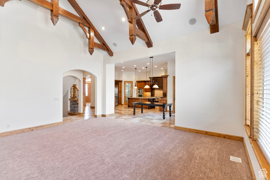 Unfurnished living room featuring ceiling fan, beamed ceiling, light carpet, and high vaulted ceiling