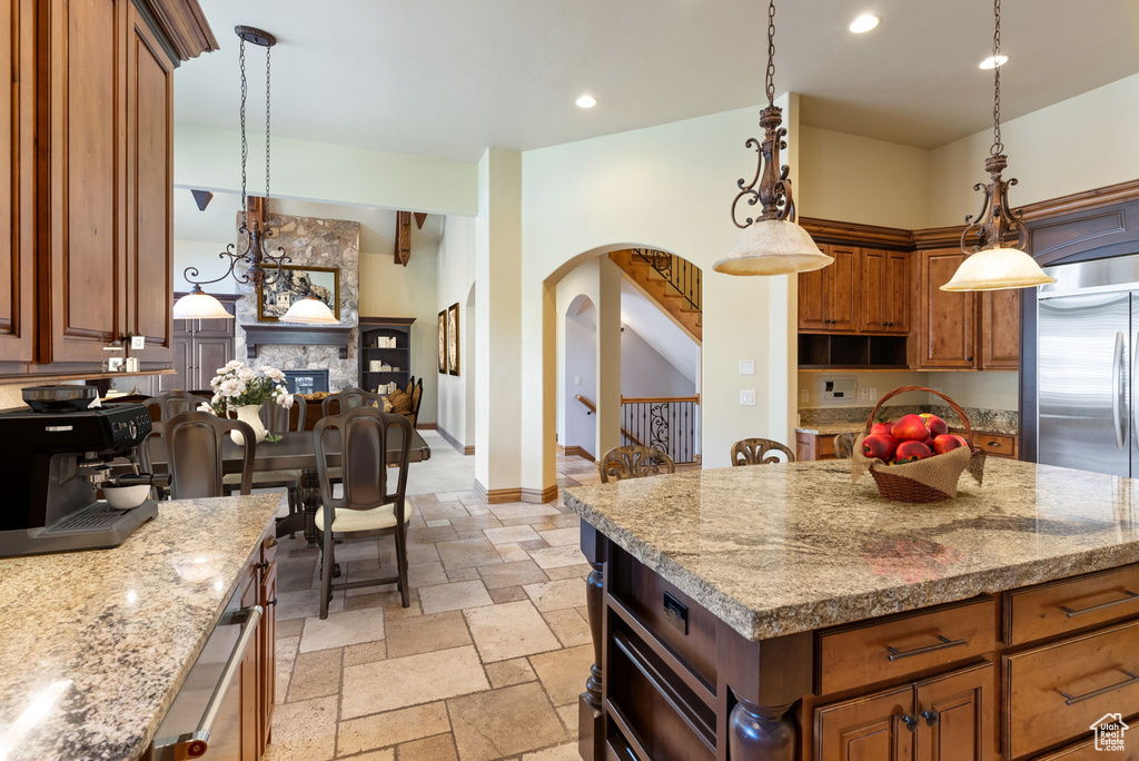Kitchen featuring light stone countertops, a kitchen island, hanging light fixtures, a fireplace, and light tile floors