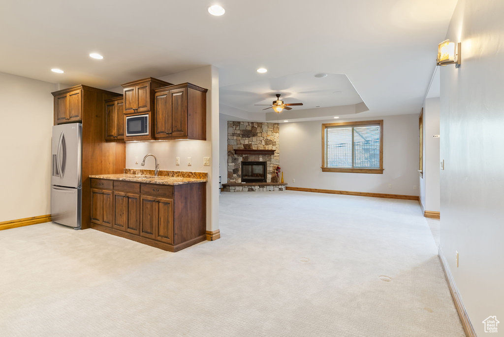 Kitchen with light carpet, a stone fireplace, stainless steel appliances, light stone countertops, and ceiling fan