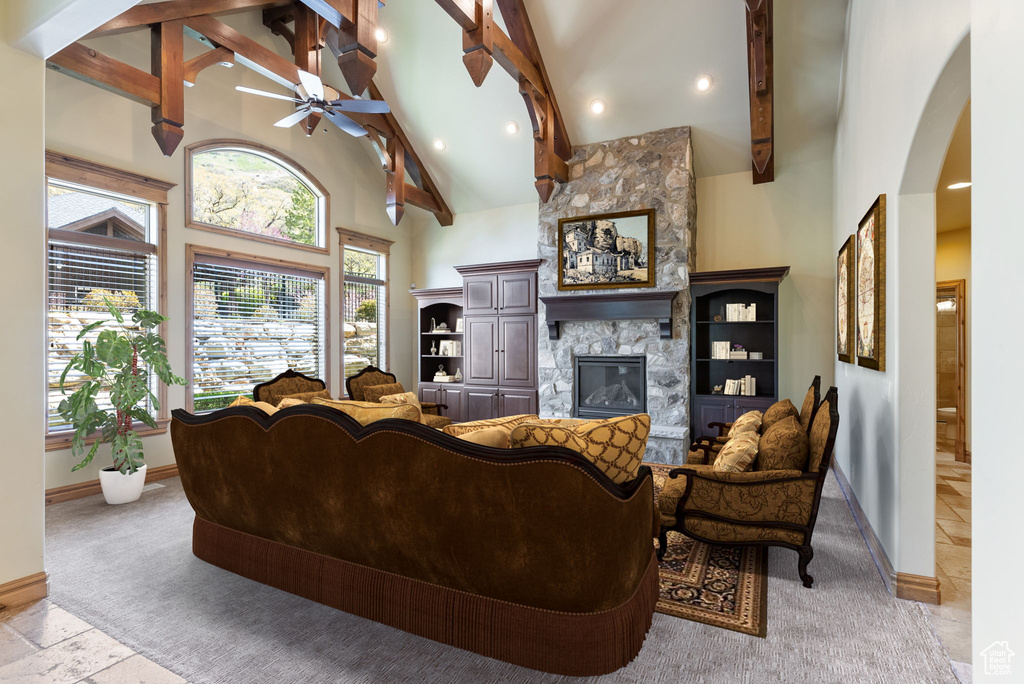 Living room with high vaulted ceiling, a stone fireplace, ceiling fan, beamed ceiling, and light tile floors