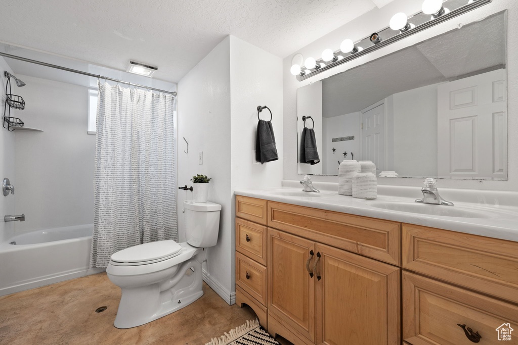 Full bathroom featuring dual bowl vanity, toilet, a textured ceiling, and shower / bath combo with shower curtain