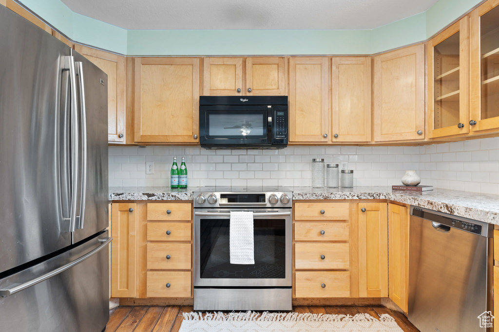 Kitchen featuring stainless steel appliances, light hardwood / wood-style floors, light stone countertops, and backsplash