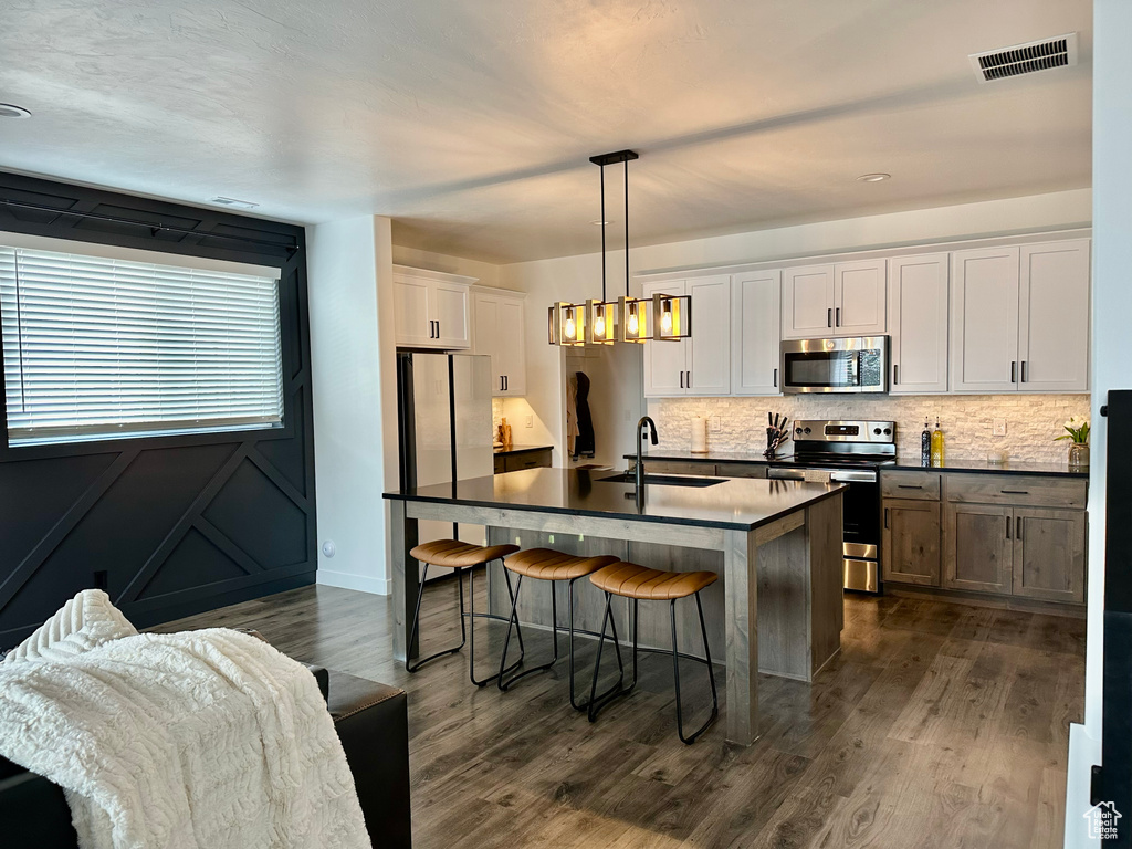 Kitchen with a kitchen island with sink, white cabinets, pendant lighting, dark hardwood / wood-style flooring, and appliances with stainless steel finishes