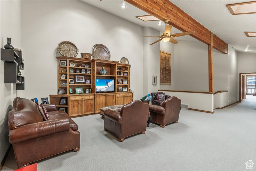 Carpeted living room featuring ceiling fan and beamed ceiling