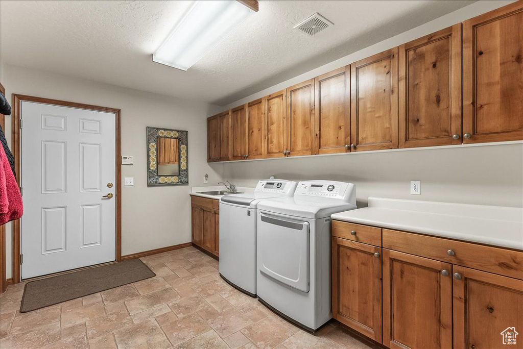 Clothes washing area with a textured ceiling, cabinets, washer and clothes dryer, light tile floors, and sink