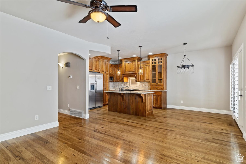 Kitchen featuring a kitchen island with sink, ceiling fan, hardwood / wood-style floors, a breakfast bar area, and stainless steel refrigerator with ice dispenser