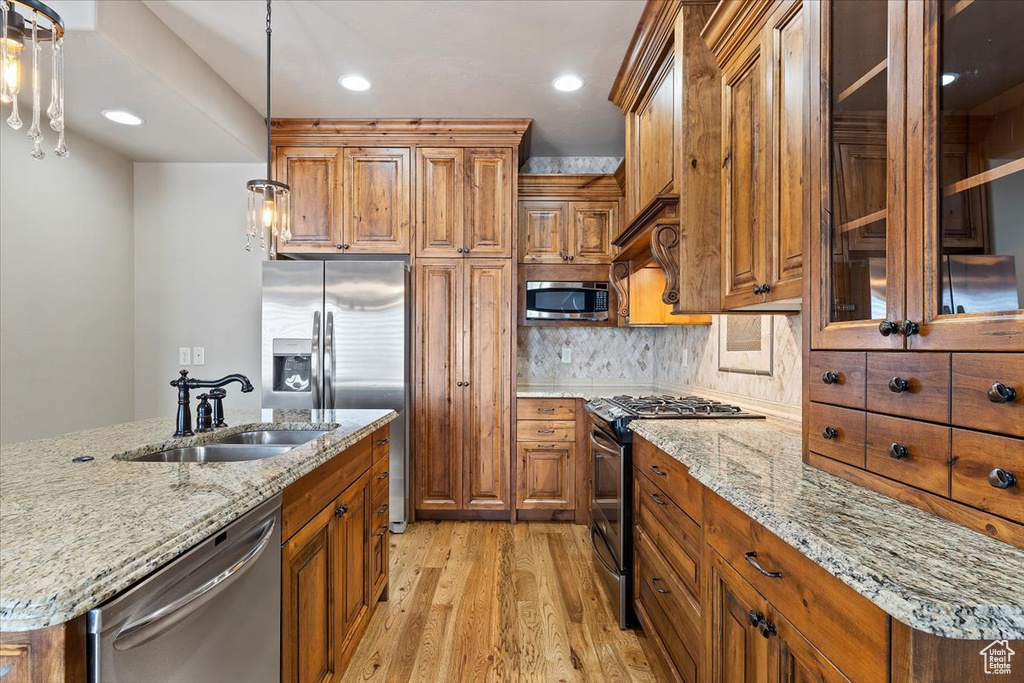 Kitchen with a kitchen island with sink, sink, decorative light fixtures, appliances with stainless steel finishes, and light wood-type flooring