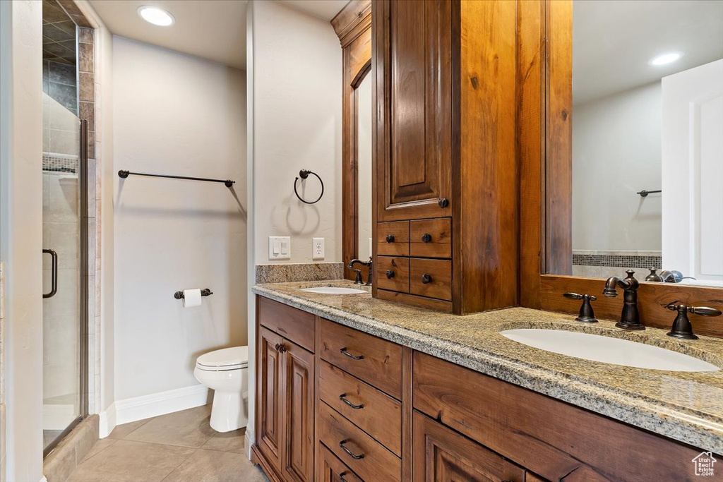 Bathroom with vanity with extensive cabinet space, tile floors, an enclosed shower, toilet, and double sink