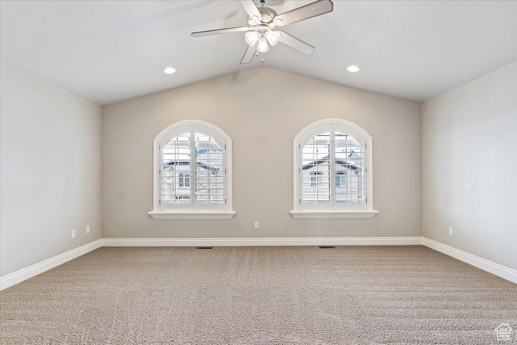 Carpeted spare room with ceiling fan, plenty of natural light, and lofted ceiling