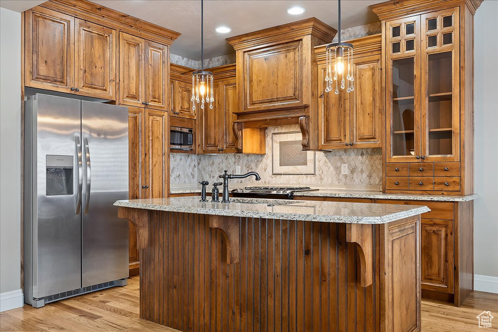 Kitchen featuring light hardwood / wood-style floors, pendant lighting, stainless steel appliances, and a breakfast bar