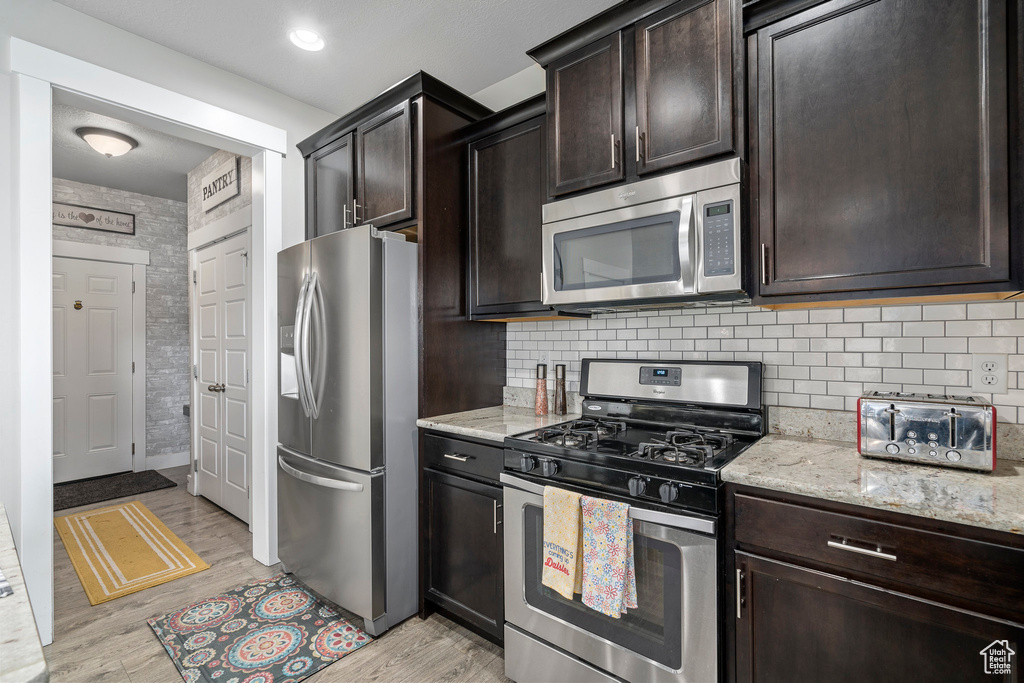Kitchen featuring appliances with stainless steel finishes, light wood-type flooring, light stone countertops, and dark brown cabinets