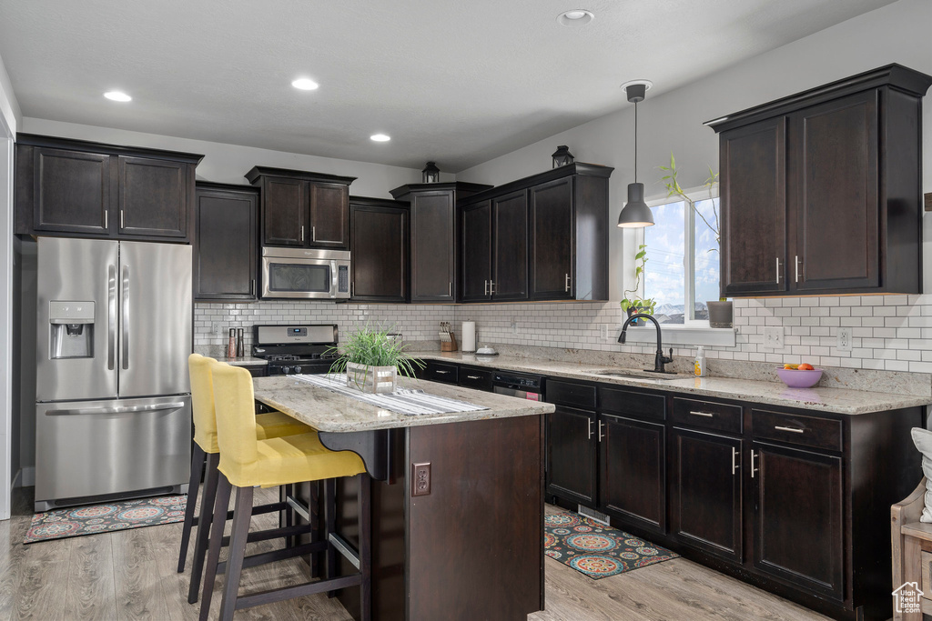 Kitchen featuring appliances with stainless steel finishes, light hardwood / wood-style floors, light stone counters, and hanging light fixtures
