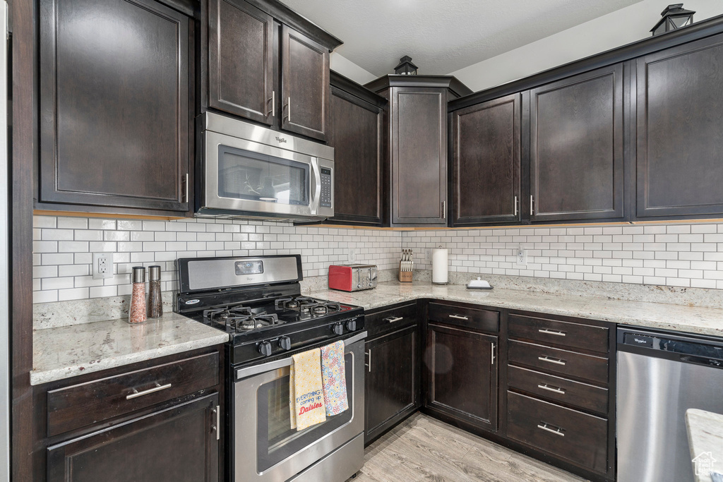 Kitchen featuring appliances with stainless steel finishes, tasteful backsplash, light hardwood / wood-style floors, and light stone counters
