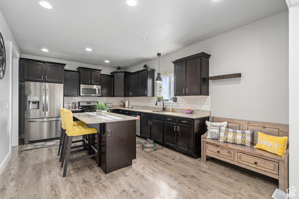 Kitchen featuring pendant lighting, light wood-type flooring, stainless steel appliances, light stone counters, and a breakfast bar area