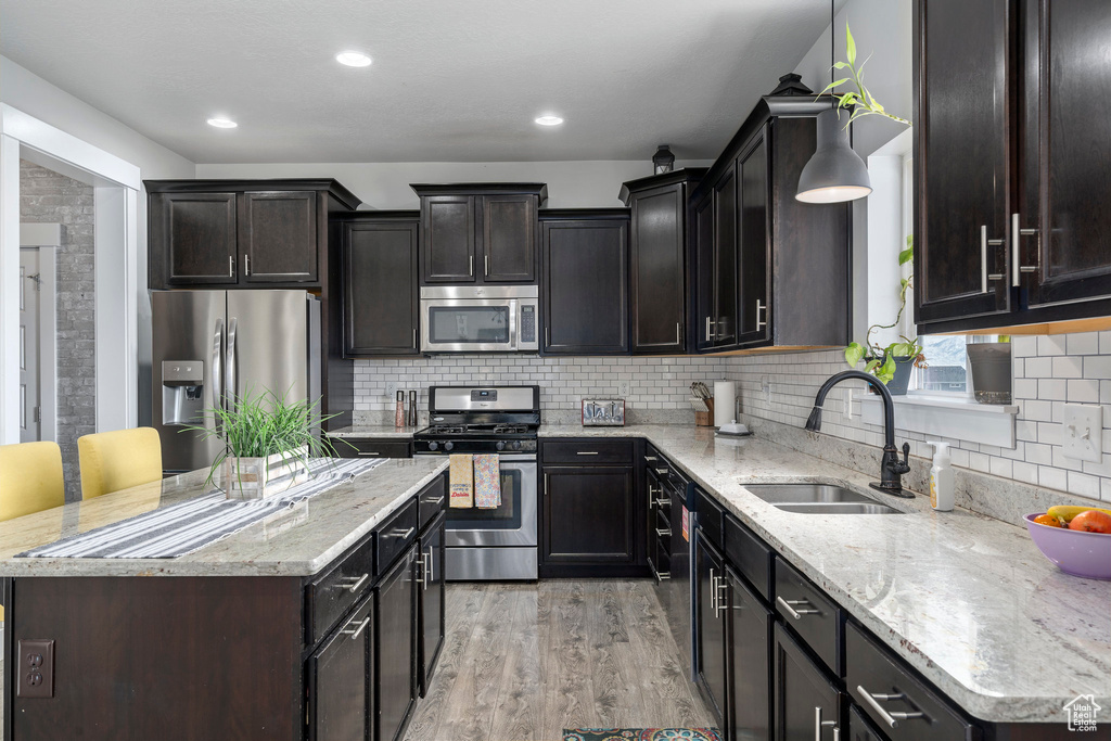 Kitchen with sink, backsplash, appliances with stainless steel finishes, light wood-type flooring, and light stone countertops