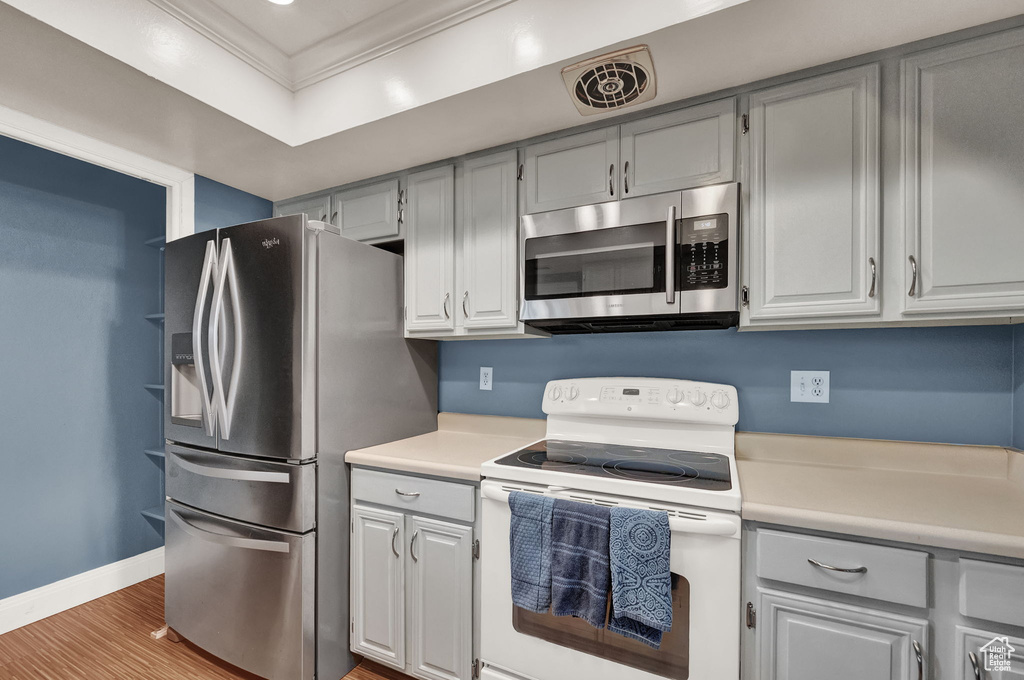 Kitchen with appliances with stainless steel finishes, gray cabinetry, crown molding, and wood-type flooring