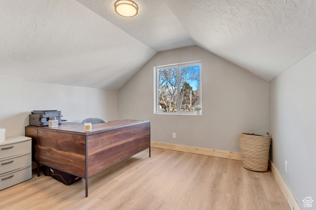 Bedroom featuring light hardwood / wood-style flooring, a textured ceiling, and vaulted ceiling