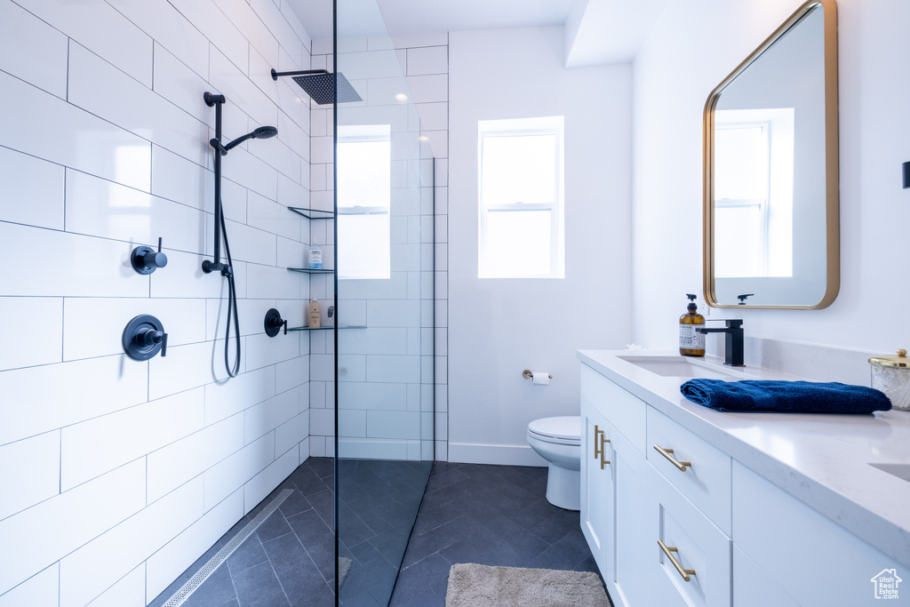Bathroom with tiled shower, oversized vanity, toilet, and tile floors