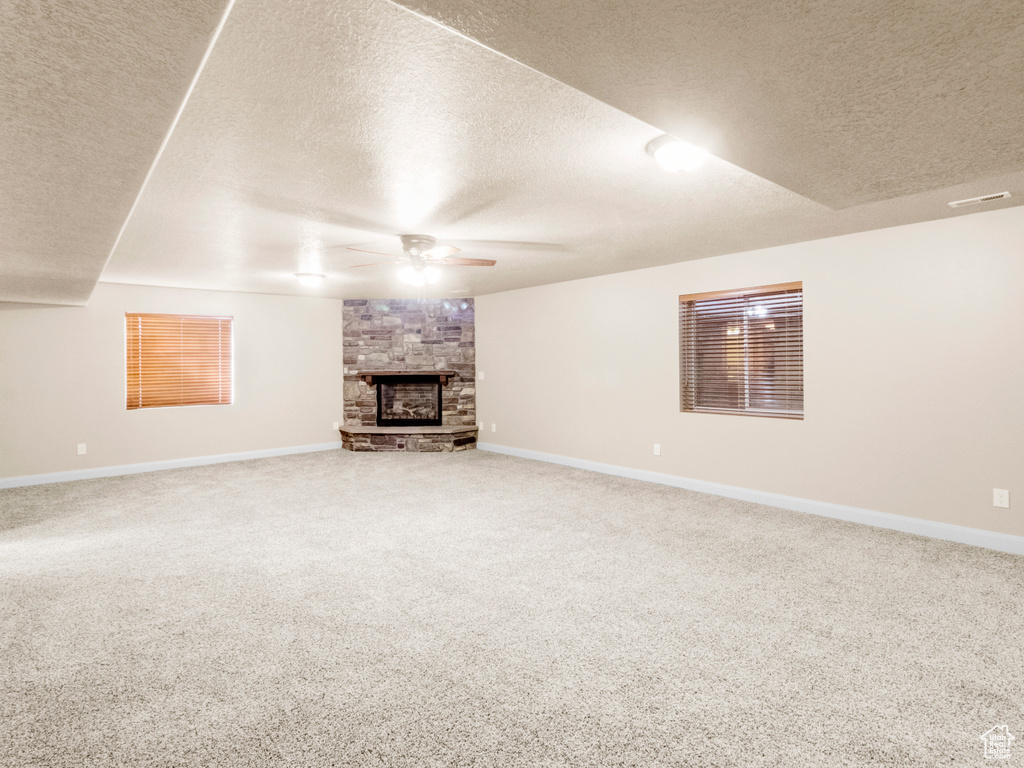 Unfurnished living room featuring a fireplace, carpet, a textured ceiling, and ceiling fan
