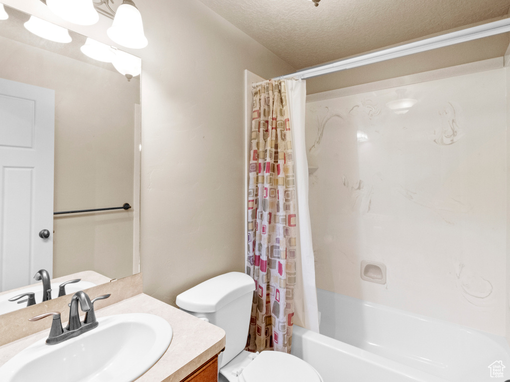 Full bathroom featuring a textured ceiling, shower / bath combo with shower curtain, toilet, and vanity