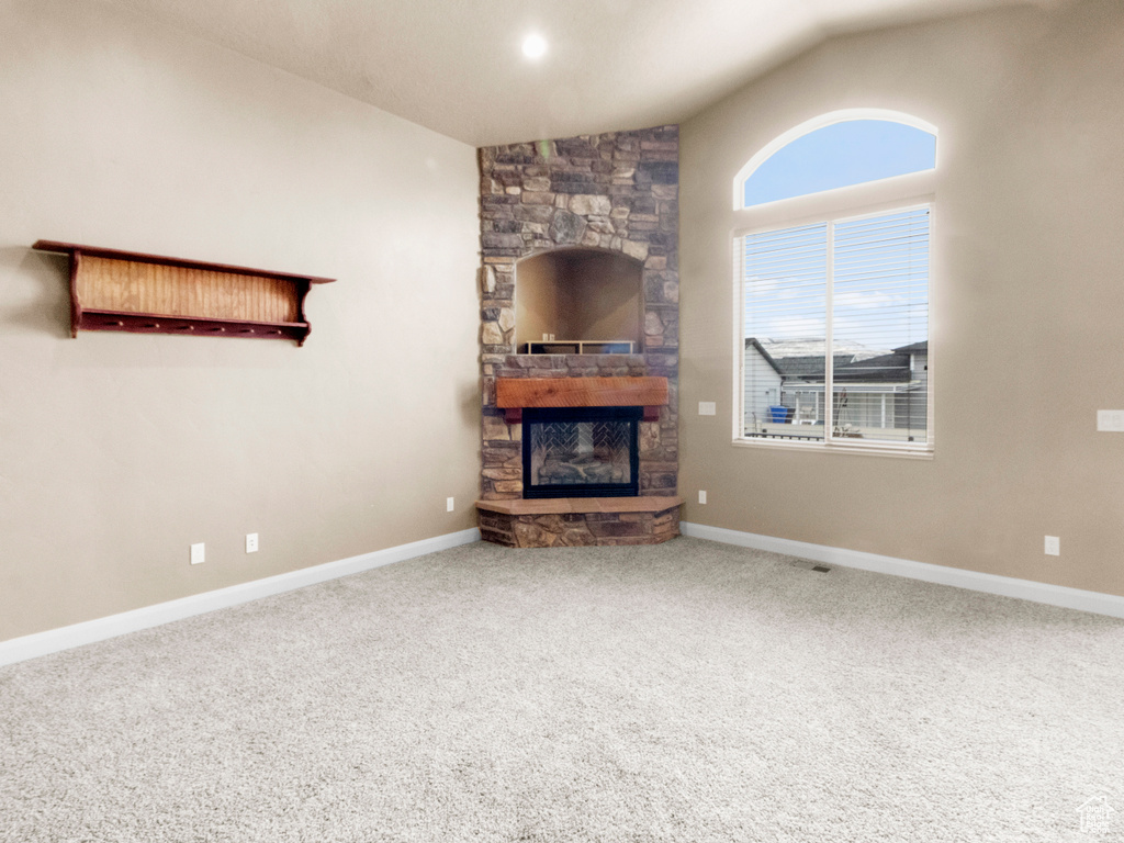 Unfurnished living room featuring lofted ceiling, a stone fireplace, and carpet flooring