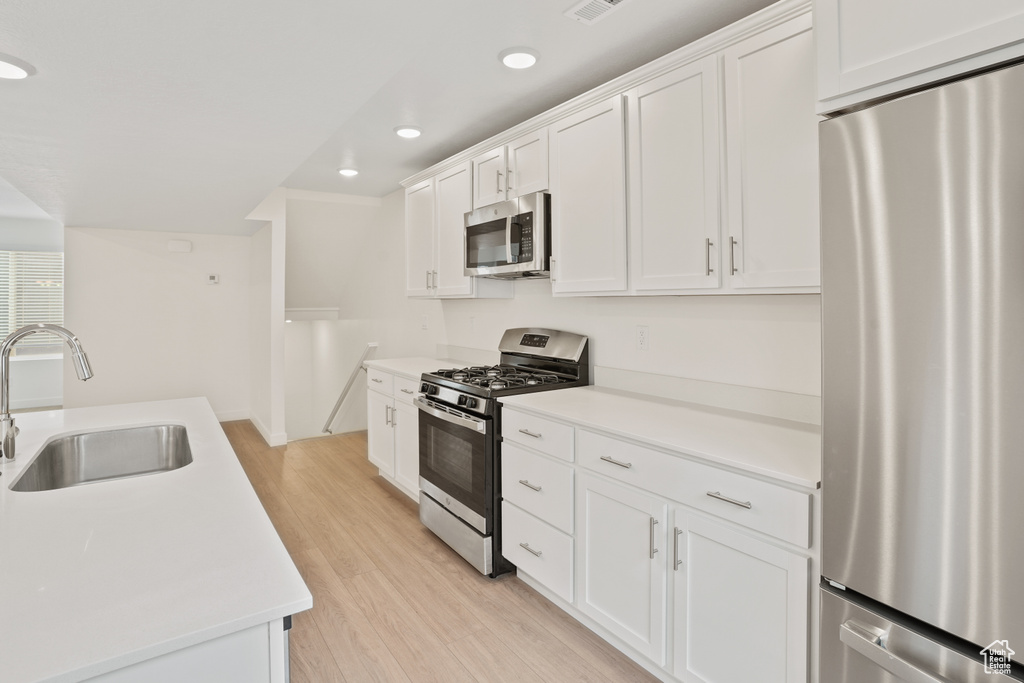 Kitchen with white cabinets, stainless steel appliances, light hardwood / wood-style floors, and sink