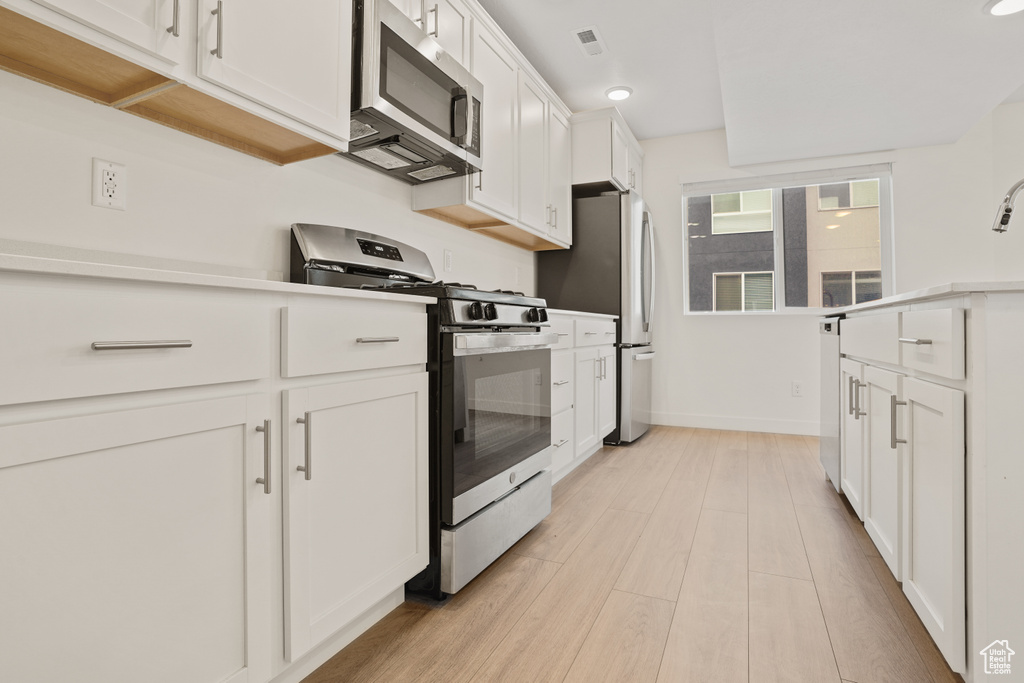 Kitchen with white cabinets, light hardwood / wood-style flooring, and stainless steel appliances