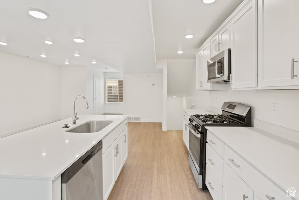 Kitchen featuring sink, white cabinets, a center island with sink, light hardwood / wood-style flooring, and stainless steel appliances