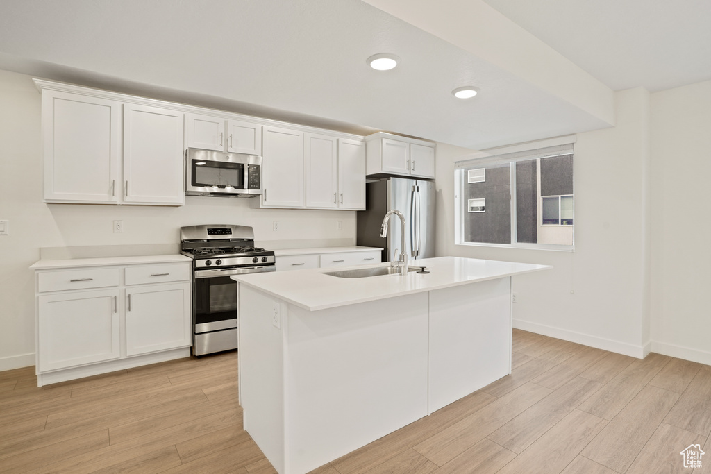 Kitchen featuring white cabinets, a center island with sink, stainless steel appliances, sink, and light hardwood / wood-style flooring